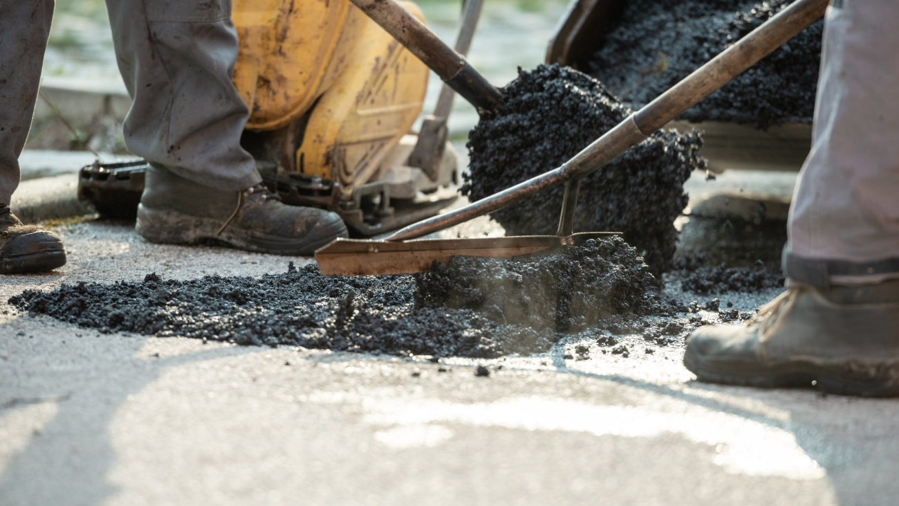 Two construction workers working together to patch a bump in the road with fresh asphalt.