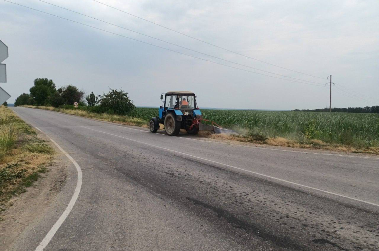 Трактор скошує траву на узбіччі дороги