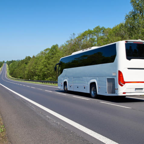 White Bus driving along an empty asphalt road lined with deciduous trees in the countryside
