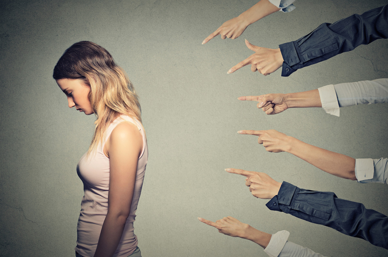Concept of accusation guilty person girl. Side profile sad upset woman looking down many fingers pointing at her back isolated on grey office wall background. Human face expression emotion feeling